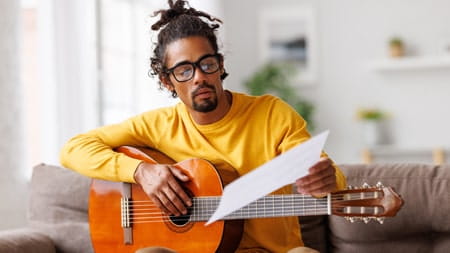 Man reading from a piece of paper while holding a guitar