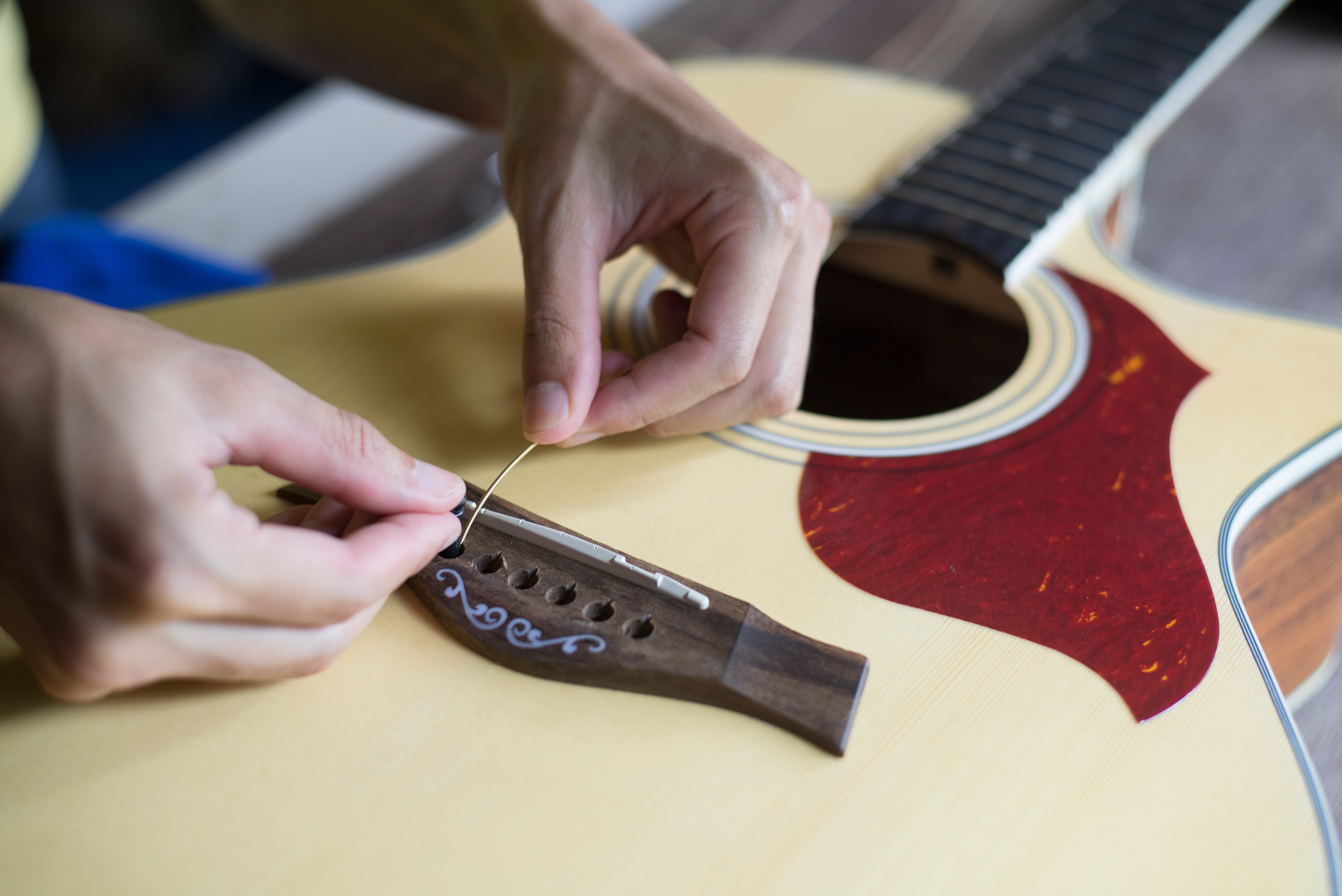 Man inserting guitar string into the bridge of an acoustic guitar.
